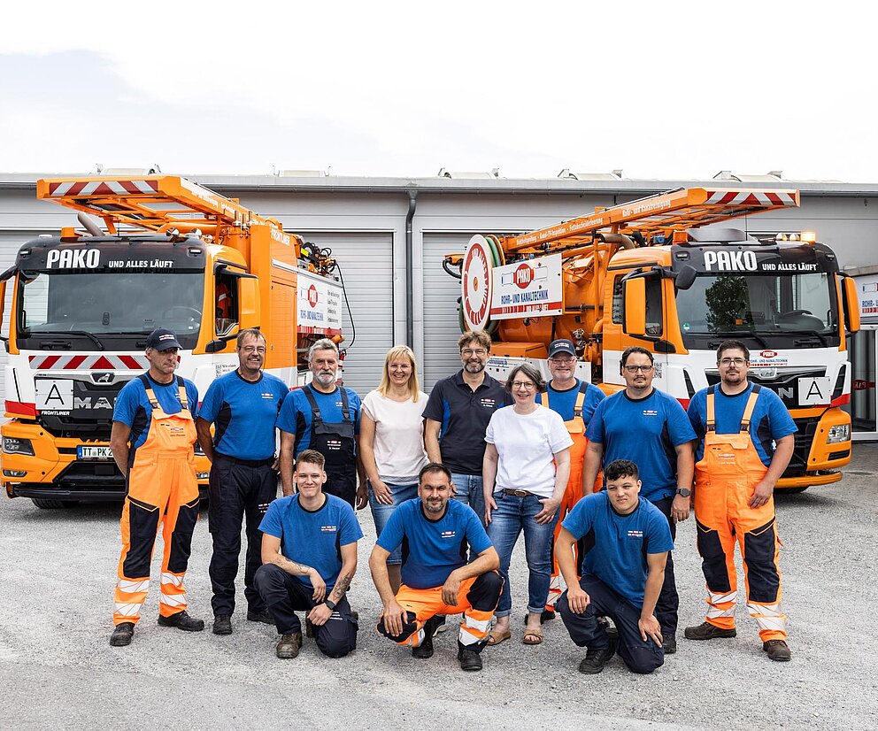 Gruppenfoto vor Einsatzfahrzeugen PAKO-Team posiert vor mehreren orangefarbenen Einsatzfahrzeugen auf dem Betriebshof.