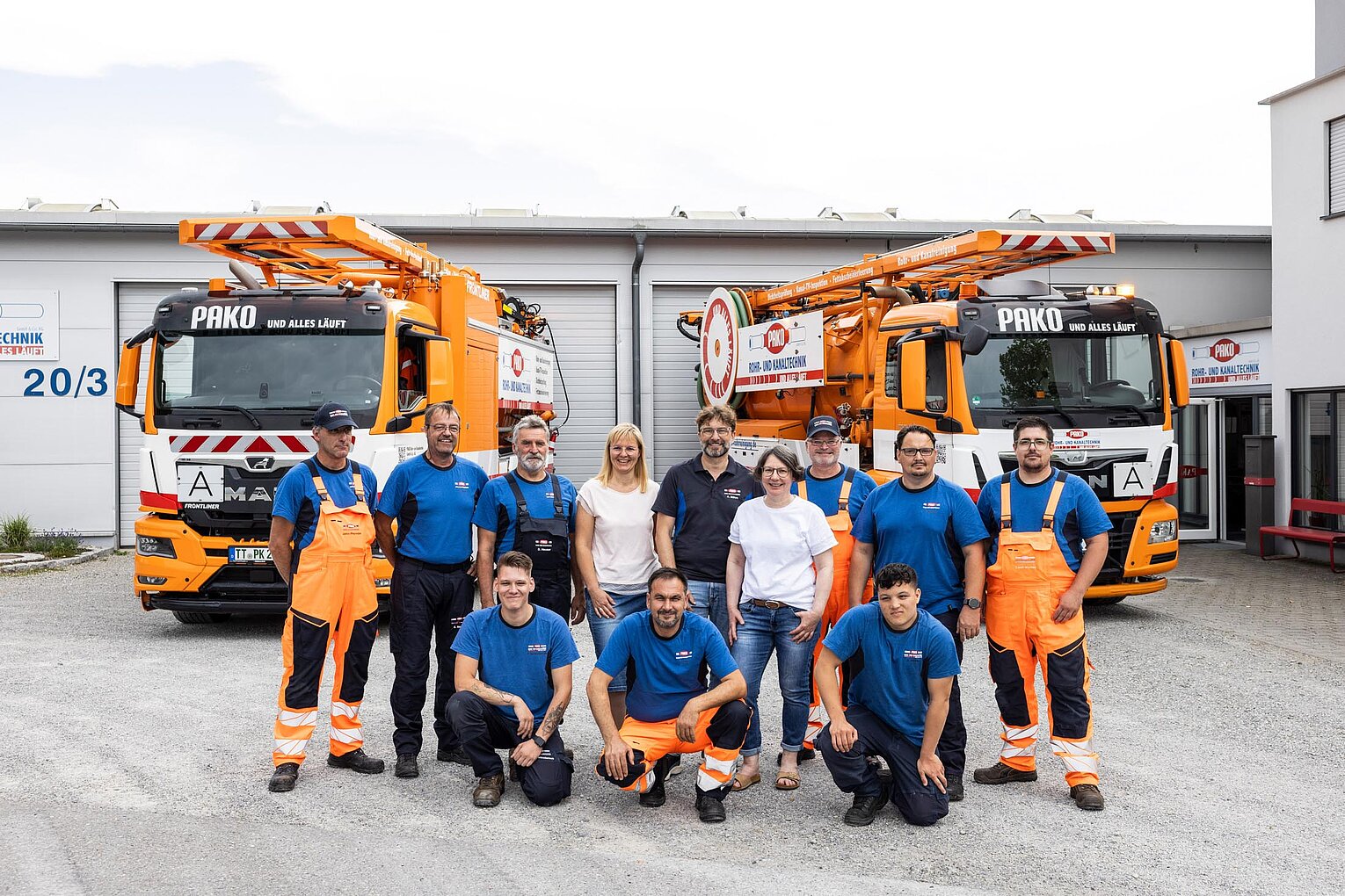 Gruppenfoto vor Einsatzfahrzeugen PAKO-Team posiert vor mehreren orangefarbenen Einsatzfahrzeugen auf dem Betriebshof.
