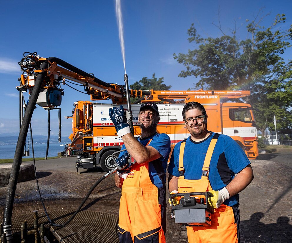 Team bei Baggerarbeiten Zwei PAKO-Mitarbeiter posieren neben einem Bagger auf einer Baustelle.