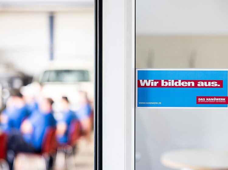 Blick in PAKO-Meetingraum PAKO-Mitarbeiter bei einer Besprechung oder Schulung im Büro; Fokus auf Tür mit PAKO-Logo und Raumbezeichnung.