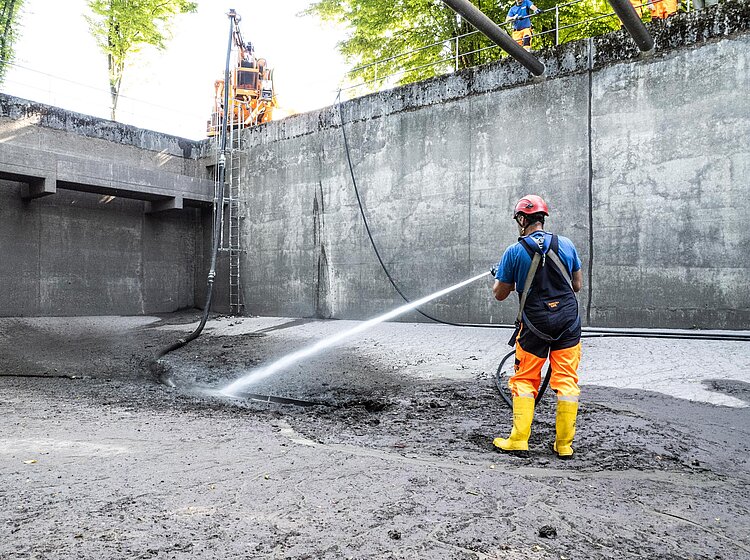 Hochdruckreinigung eines Betonbeckens PAKO-Mitarbeiter reinigt mit Hochdruckreiniger ein großes offenes Betonbecken, ausgestattet mit Schutzkleidung