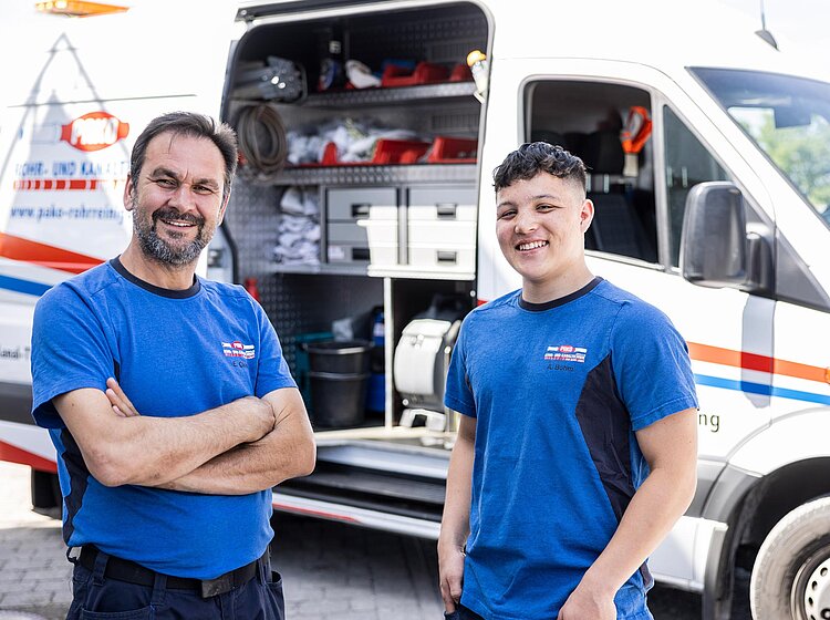 Mitarbeiter vor Servicefahrzeug Zwei PAKO-Mitarbeiter in blauer Kleidung stehen lächelnd vor einem geöffneten Servicefahrzeug mit sichtbarer Technik.