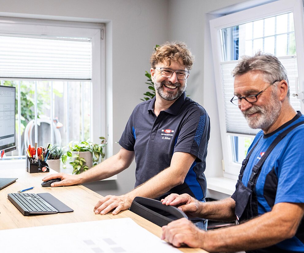 Besprechung im Büro Zwei PAKO-Mitarbeiter sitzen am Schreibtisch mit Computer und Ordnern und führen ein Gespräch.