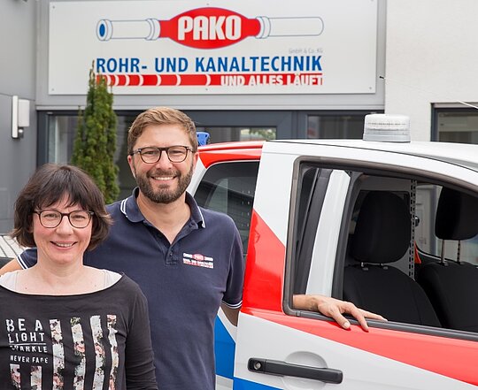 Geschäftsführer vor PAKO-Firmengebäude Zwei Mitarbeiter der PAKO Rohr- und Kanaltechnik GmbH & Co. KG stehen vor einem Firmenfahrzeug und dem Firmengebäude mit Logo.