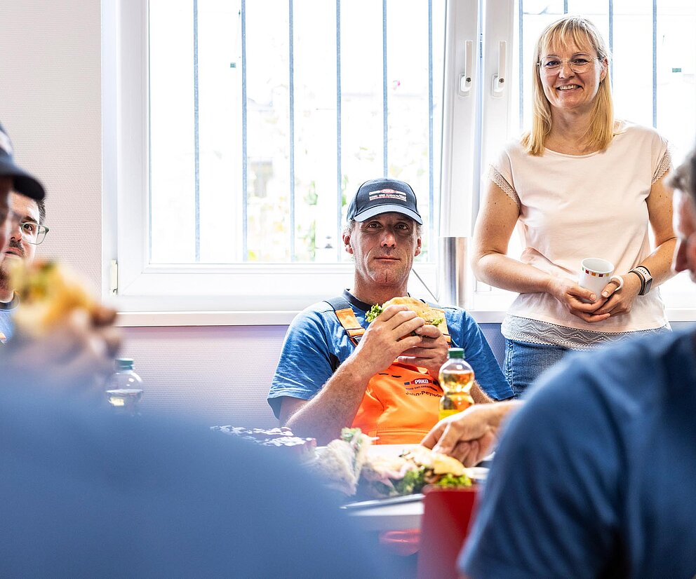 Teammeeting Schulung PAKO-Mitarbeiter sitzen in einem Besprechungsraum, Fokus auf eine Person, die zuhört.