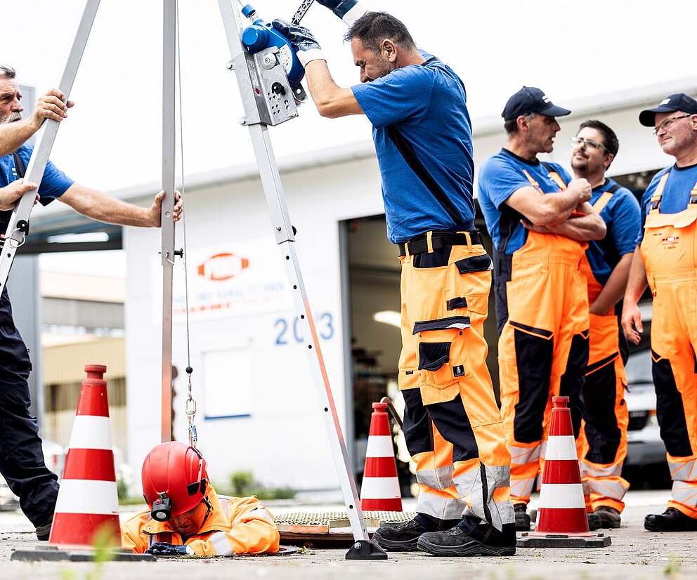 Rettungsübung mit Team PAKO-Mitarbeiter üben eine Rettungssituation mit Ausrüstung und Sicherheitsgestell, mehrere Kollegen beobachten.
