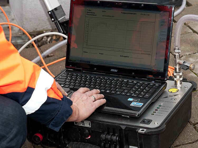 Auswertung der Dichtheitsprüfung vor Ort PAKO-Mitarbeiter in Warnweste analysiert Dichtheitsprüfungsdaten am Laptop mit angeschlossenem Messgerät.