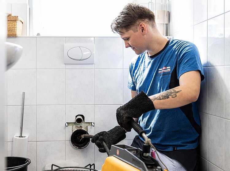 Mechanische Rohrreinigung mit Kettenschleuder PAKO-Mitarbeiter führt mechanische Rohrreinigung eines WC-Abflusses mit einer Kettenschleuder durch, Arbeitsbereich in einem Badezimmer.