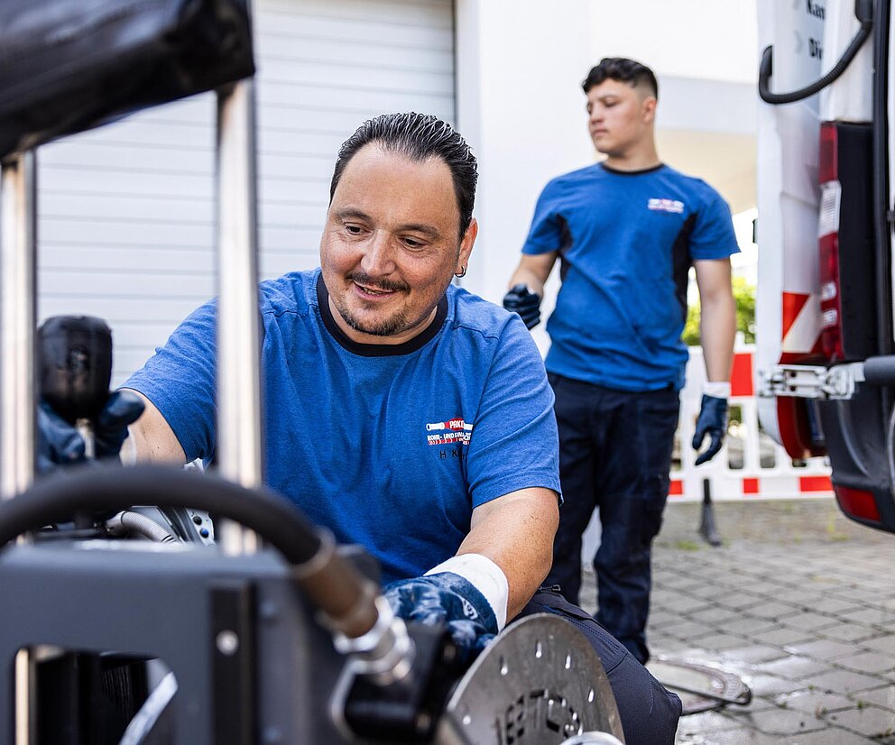 Teamfoto mit Azubi Drei PAKO-Mitarbeiter, darunter ein Azubi, posieren vor einem Servicefahrzeug.