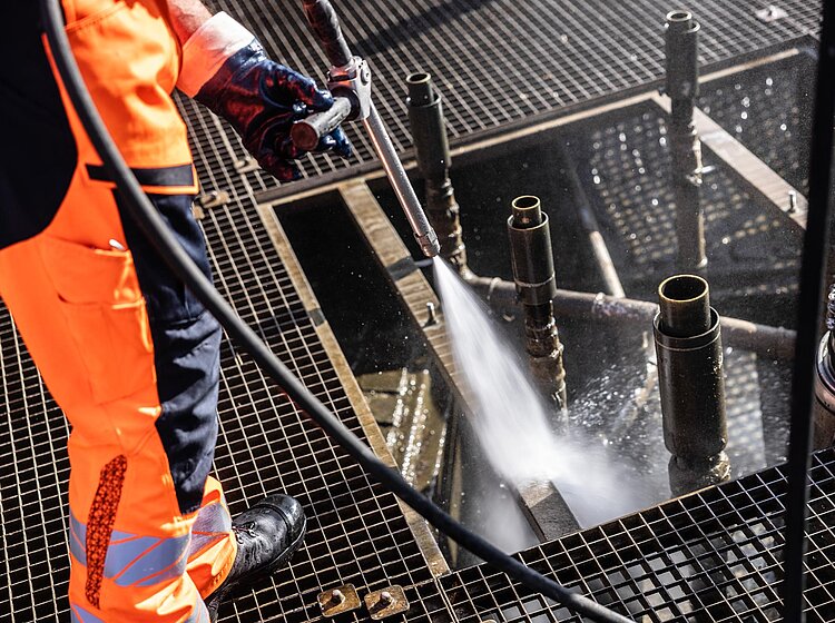 Reinigung im Schachtbereich Zwei PAKO-Mitarbeiter in oranger Schutzkleidung reinigen mit Schläuchen den inneren Bereich eines Schachtes.