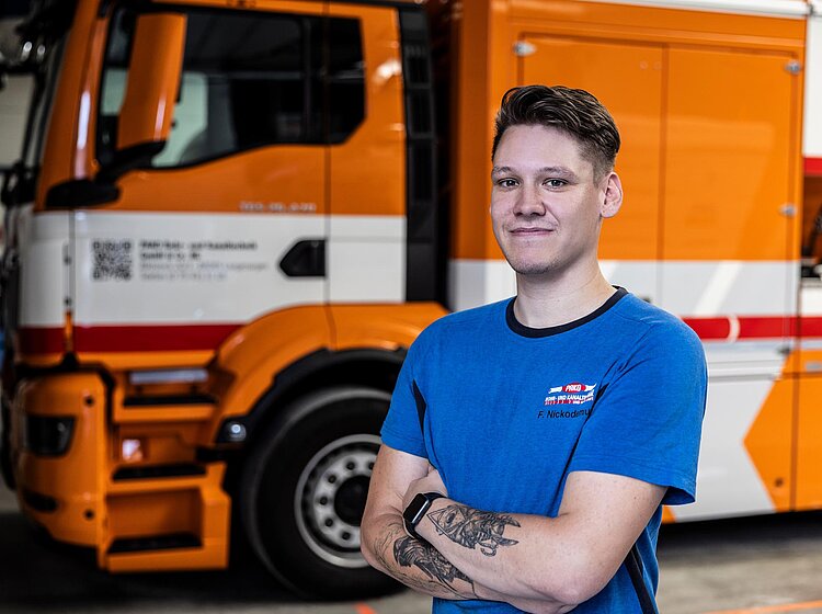 Mitarbeiter vor PAKO-Fahrzeug Junger Mitarbeiter der PAKO Rohr- und Kanaltechnik GmbH & Co. KG steht mit verschränkten Armen vor einem orangefarbenen Einsatzfahrzeug.