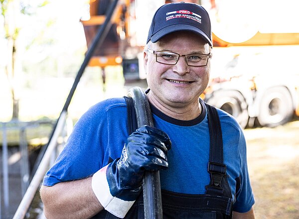 PAKO-Mitarbeiter bei der Arbeit Mitarbeiter von PAKO in Arbeitskleidung mit Schlauch vor Sauganlage, lächelt in die Kamera