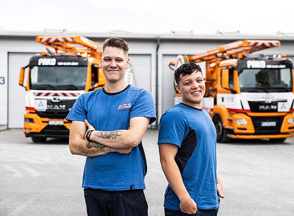 Zwei Mitarbeiter vor Saug- und Spülfahrzeugen Zwei PAKO-Mitarbeiter in blauer Arbeitskleidung posieren vor orangefarbenen Saug- und Spülfahrzeugen auf dem Betriebshof.