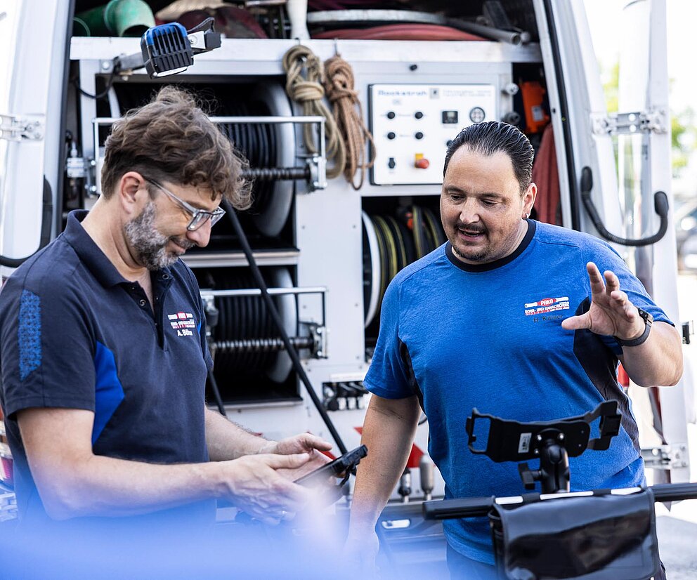 Rohrreinigung mit Einspülkamera PAKO-Mitarbeiter führen eine Rohrreinigung mit lenkbarer Einspülkamera und Wasserhochdruck durch, Kameraüberwachung sichtbar.
